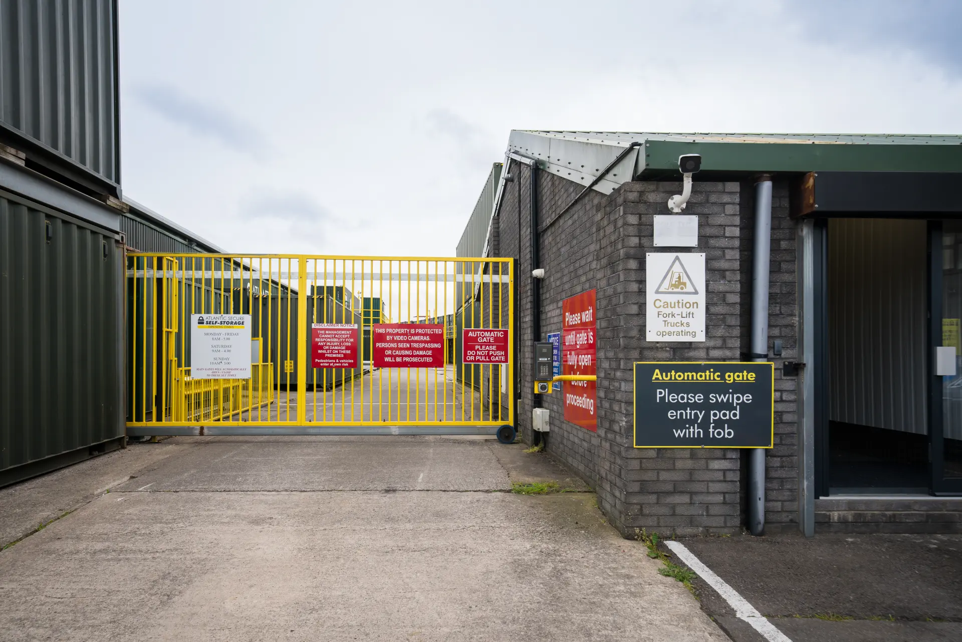 Atlantic Secure Self-Storage Barry Entrance Gate Signage 1 Yellow security gate at Atlantic Secure Self-Storage with automatic gate fob pad and warning signage
